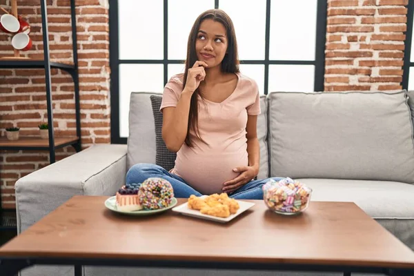 Mujer Embarazada Joven Comiendo Dulces Casa Cara Seria Pensando Pregunta — Foto de Stock