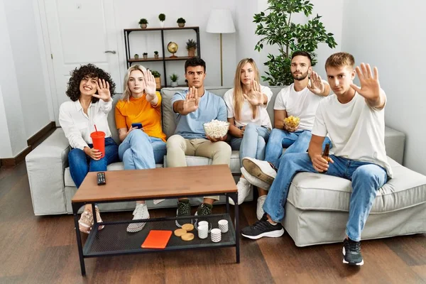 Group of people eating snack sitting on the sofa at home with open hand doing stop sign with serious and confident expression, defense gesture