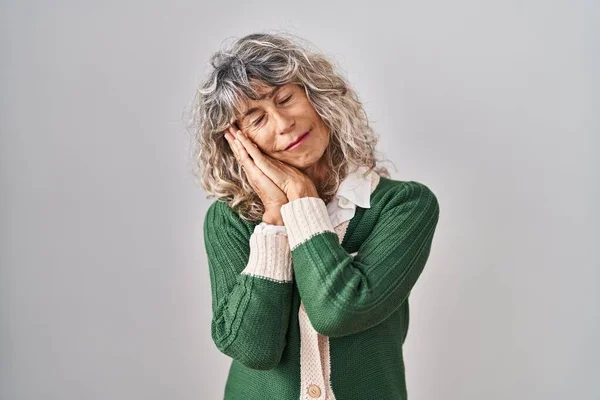 Middle age woman standing over white background sleeping tired dreaming and posing with hands together while smiling with closed eyes.