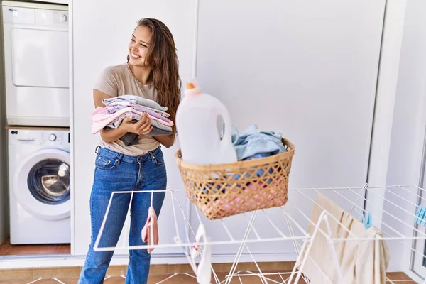 Young hispanic girl doing laundry holding folded clothes at home.