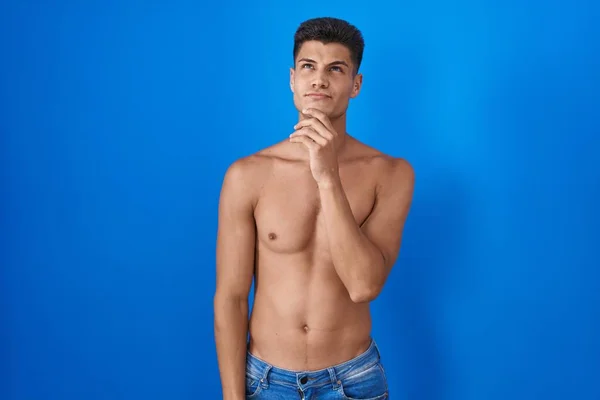 Joven Hombre Hispano Parado Sin Camisa Sobre Fondo Azul Pensando —  Fotos de Stock