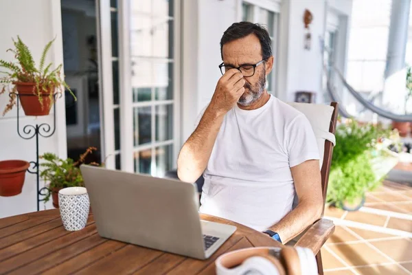 Middle age man using computer laptop at home tired rubbing nose and eyes feeling fatigue and headache. stress and frustration concept.