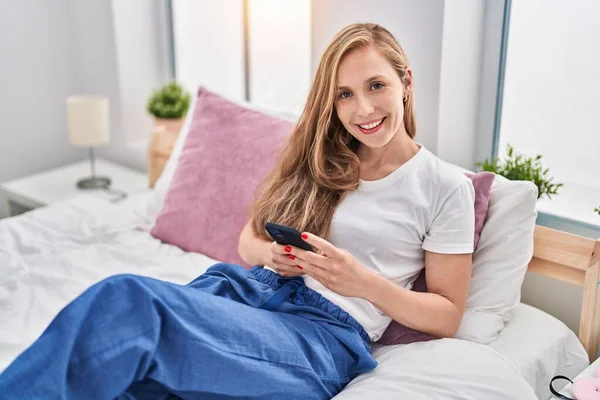 Mujer Rubia Joven Usando Teléfono Inteligente Cama Sonriendo Con Una —  Fotos de Stock