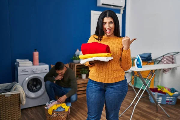 Young Couple Doing Laundry Home Pointing Thumb Side Smiling Happy — Stock Photo, Image