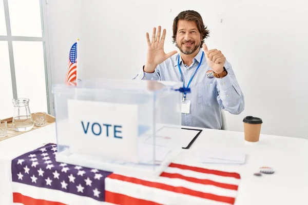 一个英俊的中年男人坐在投票站里 用六号手指指指点点着 面带微笑 自信而快乐 — 图库照片