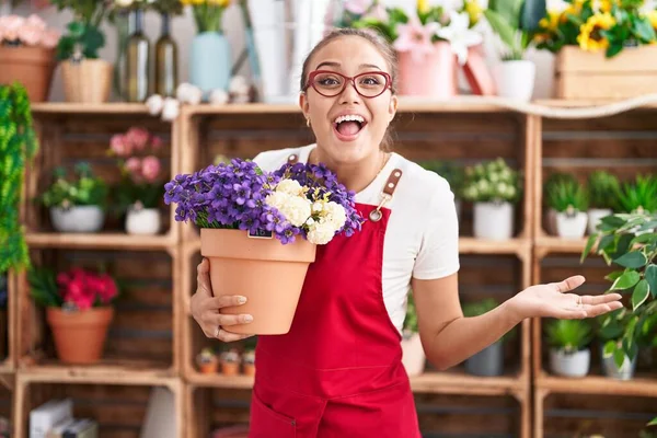 Young Hispanic Woman Working Florist Shop Holding Plant Celebrating Achievement — Stock Photo, Image