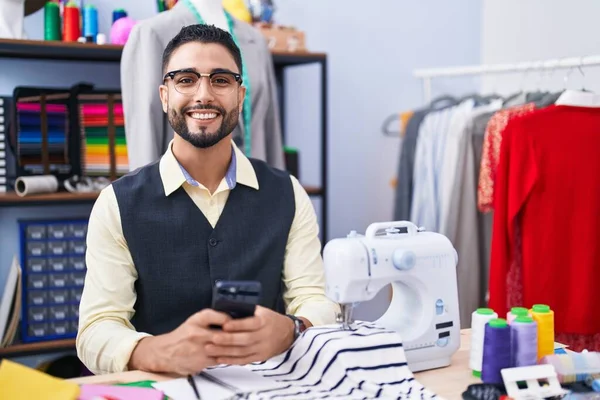 在服装厂用智能手机自信地微笑着的年轻Arab男子裁缝 — 图库照片
