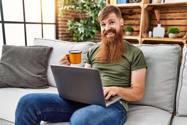 Genç Kızıl Adam Kahve Içiyor Evde Dizüstü Bilgisayar Kullanıyor — Stok fotoğraf