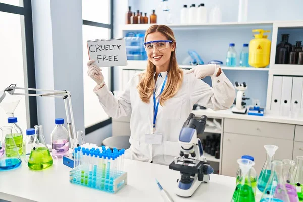 Young blonde scientist woman working on cruelty free laboratory pointing finger to one self smiling happy and proud