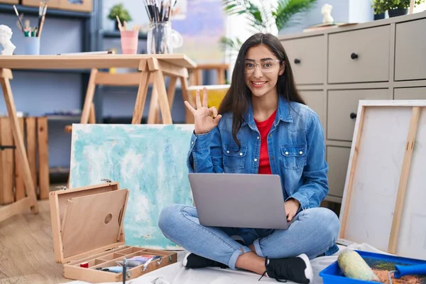 Young Teenager Girl Sitting Art Studio Using Laptop Doing Sign — Stockfoto