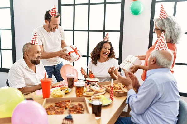 Group of middle age friends celebrate birthday giving gifts at home