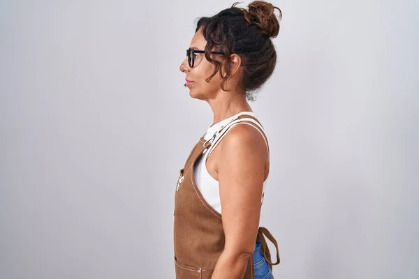Middle age woman wearing apron over white background looking to side, relax profile pose with natural face and confident smile.