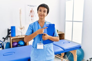 Kısa saçlı, İspanyol bir kadın. Ağrı kesici kliniğinde çalışıyor. Parmak ucunda reklamını yapıyor. 