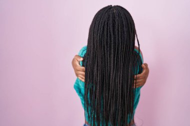 Saçları pembe arka planda dikilmiş, mutlu ve pozitif bir şekilde sarılan genç Afro-Amerikan. Sevgi ve özgüven. 