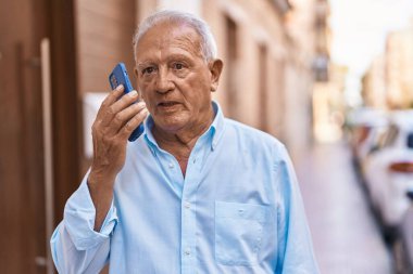 Senior grey-haired man talking on the smartphone at street