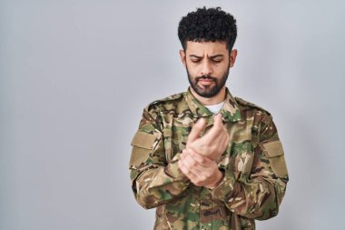 Arap adam kamuflaj üniforması giyiyor. Ellerinde ve parmaklarında ağrı var. Eklem iltihabı. 