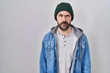 Yün şapkalı, kuşkucu ve gergin, sorun yüzünden surat asan İspanyol dövmeli genç bir adam. negatif kişi. 