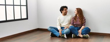 Genç İspanyol çift mutlu bir şekilde gülümsüyor ve boş bir evde yerde oturuyor..