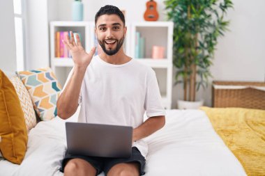 Laptop kullanan İspanyol genç adam mutlu bir gülümsemeyle zaferi kutluyor ve ellerini kaldırarak kazanıyor. 