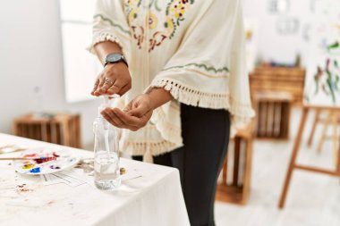 Genç İspanyol kadın sanat stüdyosunda dezenfektan jel kullanıyor.