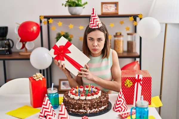 西班牙裔女人抱着礼物的怀疑和紧张庆祝生日 皱着眉头因为问题而难过 消极的人 — 图库照片