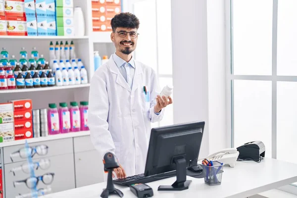 Jovem Hispânico Homem Farmacêutico Segurando Pílulas Garrafa Usando Computador Farmácia — Fotografia de Stock