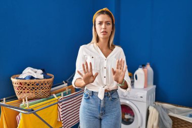Çamaşır odasındaki genç sarışın kadın elleri hareket ediyor. Avuçlarını kaldırıyor. Korkmuş ve iğrenç bir ifadeyle reddediyor. Dur ve yasakla. 