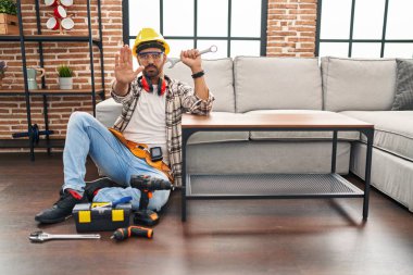 Sakallı ve sakallı genç adam hareket servisi üzerinde çalışıyor. Eli açık, dur işareti yapıyor. Ciddi ve kendinden emin bir ifadeyle, savunma jesti. 