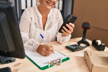 Orta yaşlı kadın ecommerce iş işçisi. Ofisteki panoya akıllı telefon yazısıyla yazıyor.