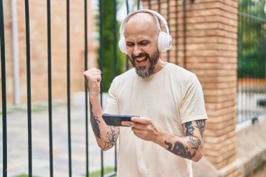 Genç kel adam gülerek sokakta video oyunu oynuyor.