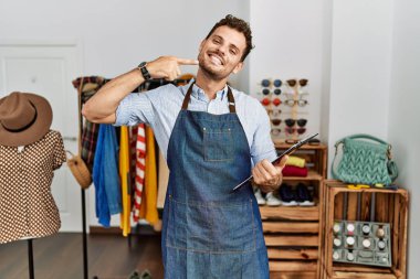 Perakende mağazasının müdürü olarak çalışan yakışıklı genç adam neşeli bir şekilde gülümseyip parmaklarını ve ağzını işaret ediyor. diş sağlığı kavramı. 