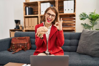 Muayenehanedeki genç esmer kadın elinde beyin tutuyor. Parmaklarıyla imza atıyor, gülümseyerek mükemmel bir sembol oluşturuyor. 