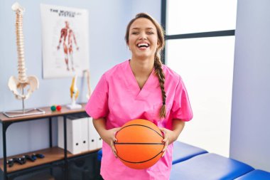 Fizyoterapi kliniğinde çalışan genç İspanyol bir kadın basketbol topu tutuyor ve kahkahalarla gülüyor.. 
