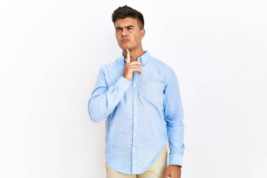 İş gömleği giyen genç İspanyol bir adam izole edilmiş arka planda durup parmak çenede şüpheye odaklanmış ve yukarı bakıp merak ediyordu. 