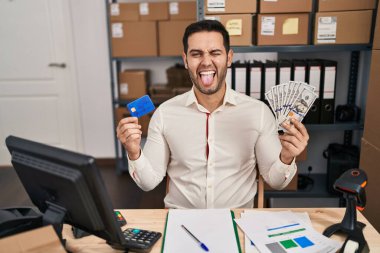 Sakallı genç İspanyol bir adam küçük bir iş yerinde çalışıyor elinde banknotlar ve kredi kartı var komik bir ifadeyle dilini dışarı çıkarıyor.. 