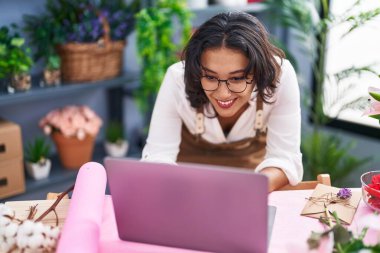 Young beautiful hispanic woman florist smiling confident using laptop at flower shop
