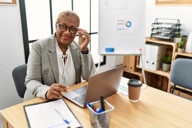Ofiste çalışan üst düzey Afro-Amerikan iş kadını laptopu kullanıyor.
