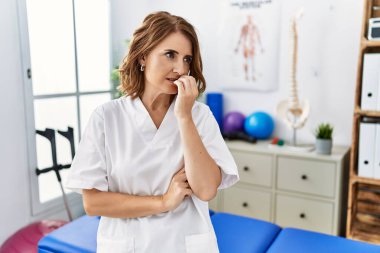 Ağrı kesici kliniğinde çalışan orta yaşlı fizyoterapist kadın elleri ağız yiyen tırnaklarla stresli ve gergin görünüyor. anksiyete. 