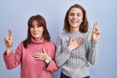 Anne ve kızı mavi arka planda durup gülümsüyor, el ve göğüste yemin ediyor, sadakat yemini ediyorlar. 