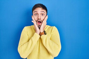 Mavi arka plan üzerinde duran İspanyol adam korkmuş ve şok olmuş, şaşırmış ve şaşırmış bir yüz ifadesi var. 