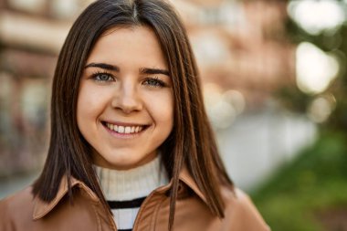 Genç, güzel, esmer kadın dışarıda mutlu bir şekilde gülümsüyor.