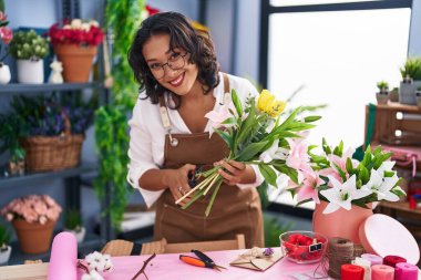 Young beautiful hispanic woman florist make bouquet of flowers at flower shop