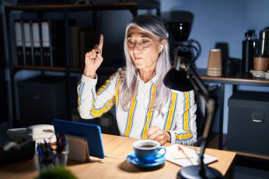 Geceleri ofiste çalışan gri saçlı orta yaşlı bir kadın başarılı bir fikirle işaret ediyor. Heyecanlı ve mutlu. Bir numara.. 