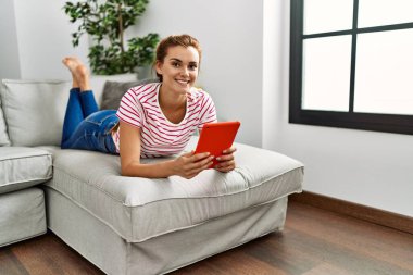 Evdeki kanepede uzanmış dokunmatik ped kullanan genç bir kadın.