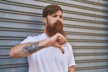 Genç kızıl saçlı adam sokağın aşağısında negatif işaret veriyor.