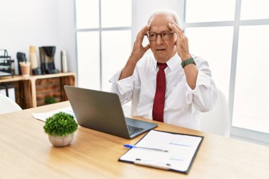 Ofiste çalışan kıdemli bir adam elleri başının üstünde bilgisayar kullanıyor. Stres yüzünden başı ağrıyor. migren ağrısı. 
