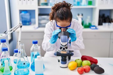 Middle age hispanic woman looking through microscope at laboratory