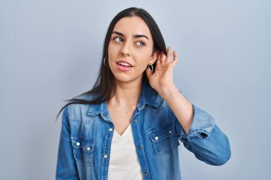 Mavi arka planda dikilen İspanyol kadın kulağına fısıldayarak dedikoduları ve dedikoduları dinliyor. Sağırlık kavramı. 