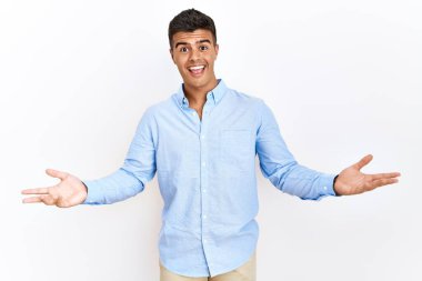 İş gömleği giyen genç İspanyol adam izole edilmiş arka planda neşeli bir şekilde gülümseyerek dostça karşılanıyor, olumlu ve kendinden emin selamlar. 