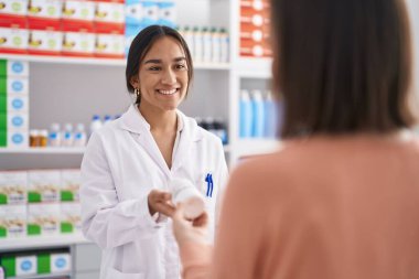 Two women pharmacist and customer holding pills bottle at pharmacy